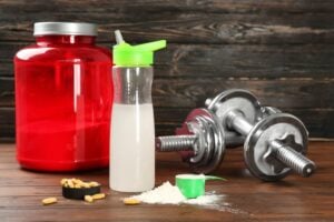 Composition with protein powder, shake and dumbbells on wooden background
